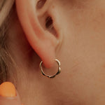 A close-up image of a girl's ear wearing a gold-colored hoop earring with a floral design.