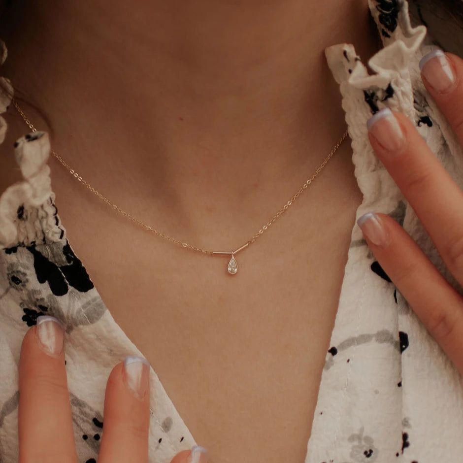 Gold necklace with a teardrop pendant worn by a person