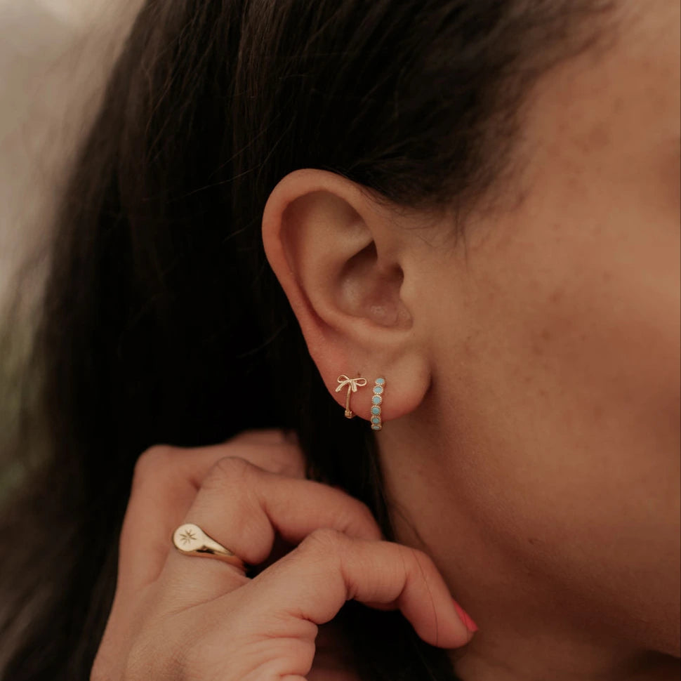 Close-up of an ear with a gold earring and ring, with a blurred background.