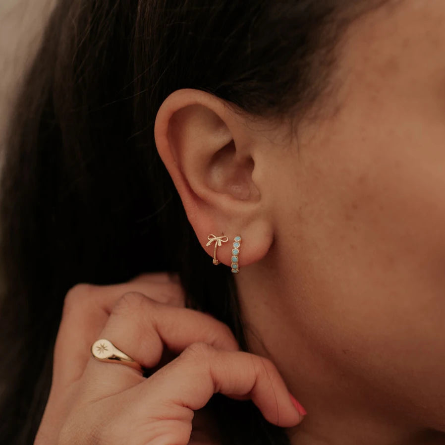 Close-up of an ear wearing a gold earring with small stones, with a hand holding a gold ring.