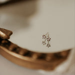 A single floral design mini stud earring placed on a white surface with a blurred background.