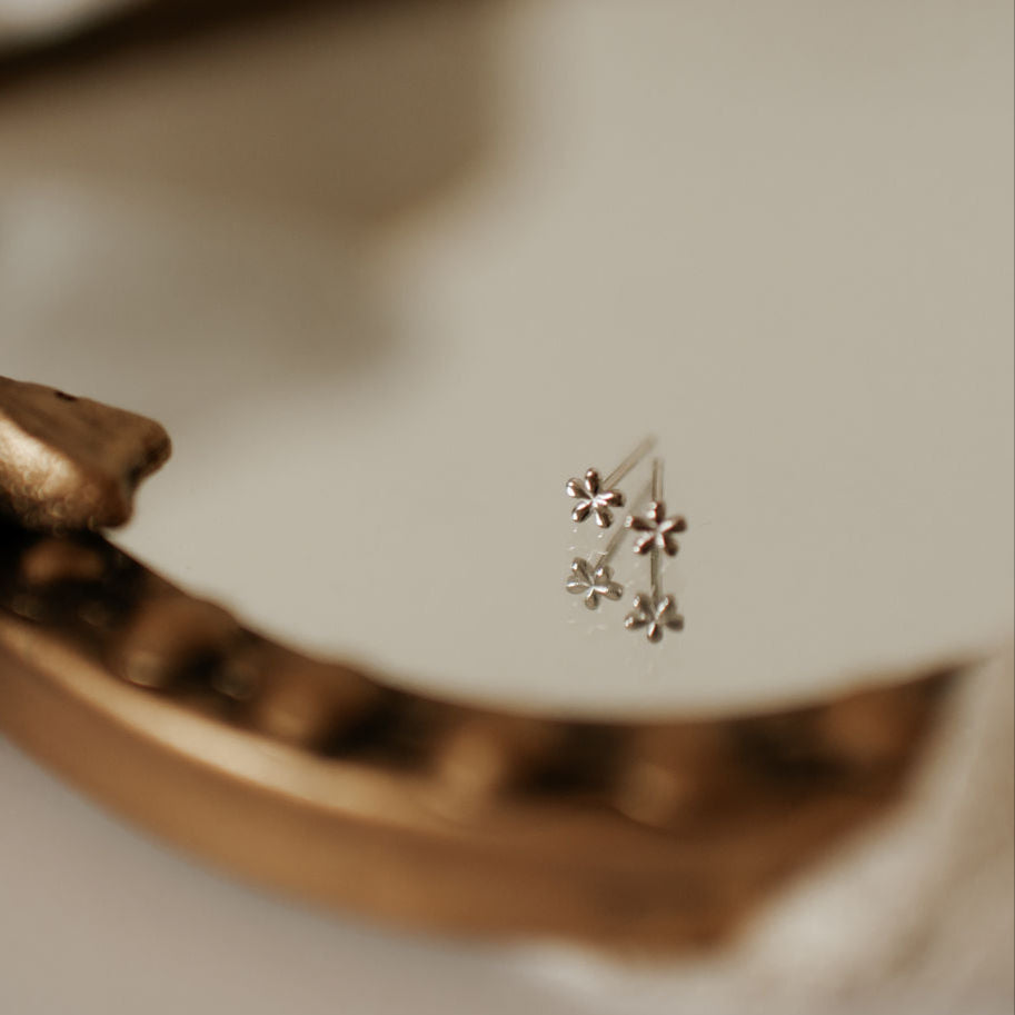 A single floral design mini stud earring placed on a white surface with a blurred background.