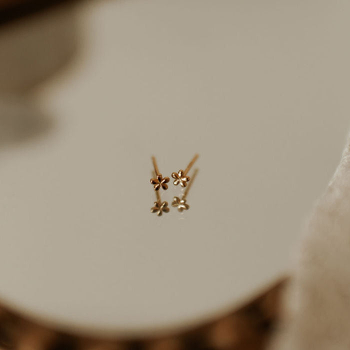 A pair of small, gold vermeil stud earrings with a floral design, displayed against a soft-focused background.