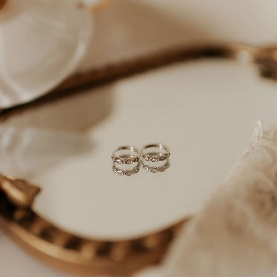 Two silver earrings on a decorative plate with a blurred background