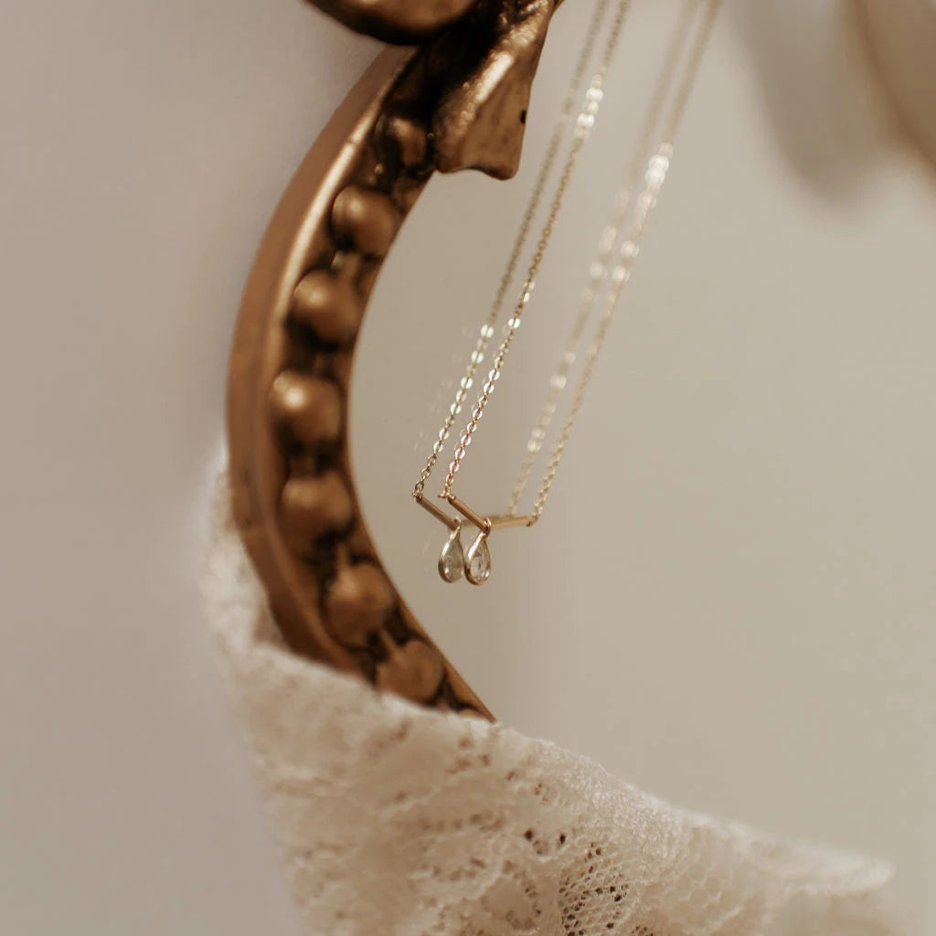 Gold necklace with a teardrop pendant on a textured surface