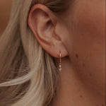 Close-up of an ear wearing a gold earring with a small gemstone.