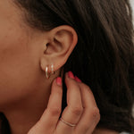 Close-up of an ear with gold hoop earrings and a hand adjusting them.