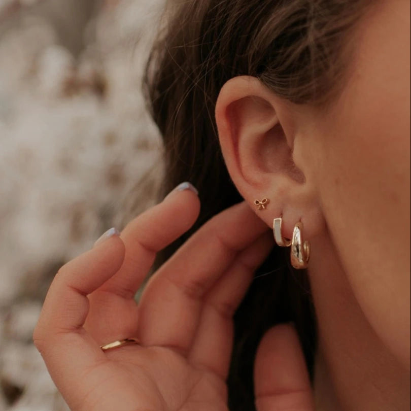 Close-up of an ear wearing gold hoop earrings with a blurred natural background