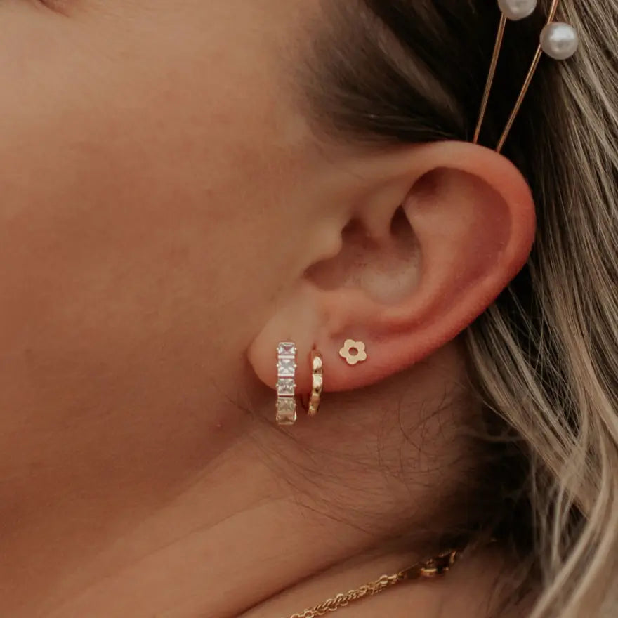 Close-up of an ear with gold earrings and hairpins.