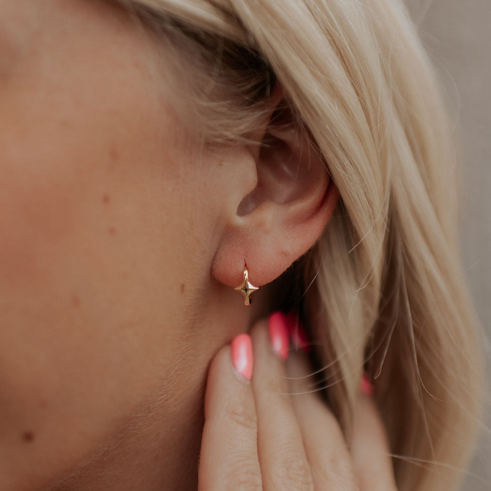 Close-up of a person wearing a gold star-shaped earring with blurred background