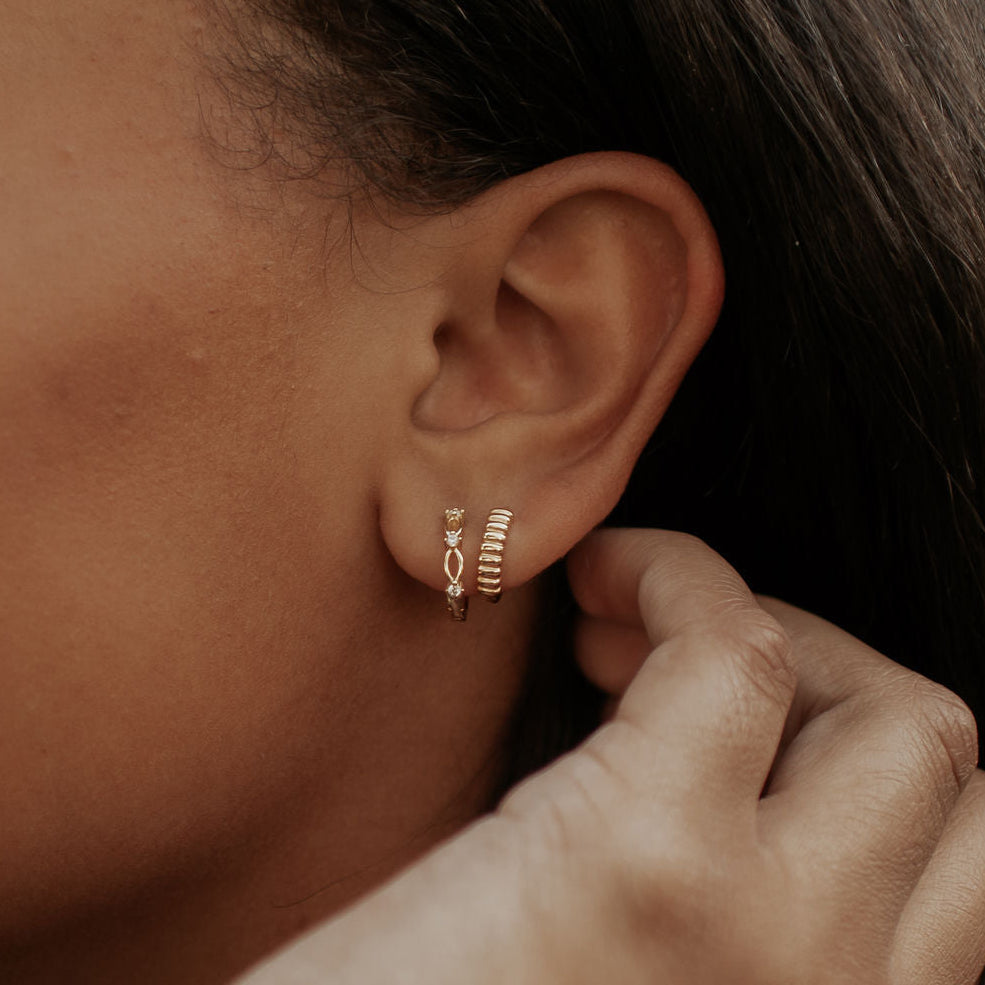Close-up of an ear wearing a gold hoop earring with a blurred background