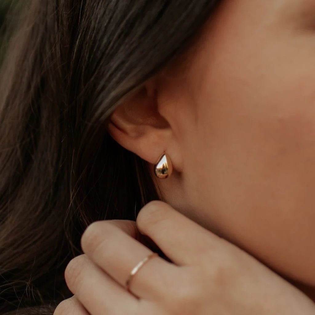 Close-up of a person wearing a gold teardrop earring with a blurred background