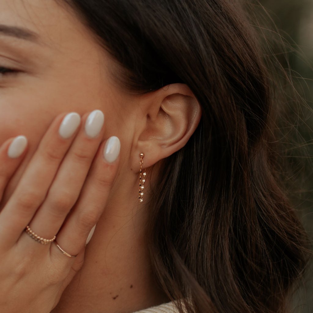 Close-up of a woman's ear with a pearl earring, hand covering face, and rings on fingers.