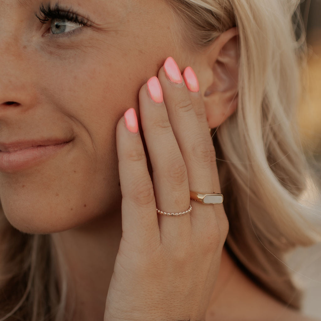 Close-up of a woman with blonde hair touching her ear, wearing a ring.