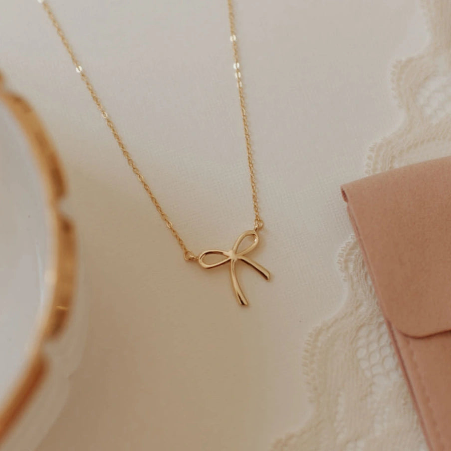 Gold bow-shaped necklace on a soft beige background