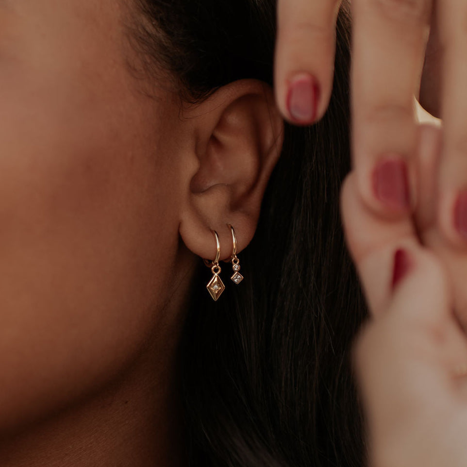 Close-up of a person wearing gold hoop earrings with a blurred background
