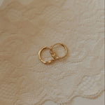 Gold hoop earrings on a textured beige surface