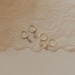 Gold and silver hoop earrings on a textured beige fabric background