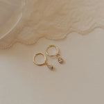 Gold hoop earrings with teardrop-shaped charms on a lace fabric background