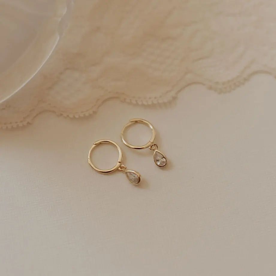 Gold hoop earrings with teardrop-shaped charms on a lace fabric background