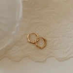 Gold hoop earrings on a textured beige fabric background