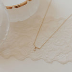 Gold necklace with a small pendant on a textured beige surface