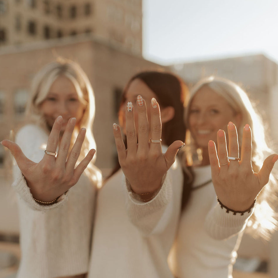 Three women holding up their hands with rings on a city street.