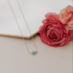 Load image into Gallery viewer, Necklace with a blue gemstone on a white surface with pink flowers.
