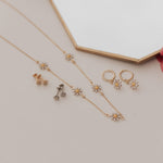 Load image into Gallery viewer, Gold jewelry set with necklace and earrings on a light surface with a pink rose.
