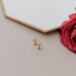 Load image into Gallery viewer, Gold daisy earrings on a light surface with a red flower and hexagonal mirror in the background
