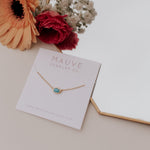 Load image into Gallery viewer, Gold necklace with a blue stone on a Mauve Jewelry Co. card with flowers in the background
