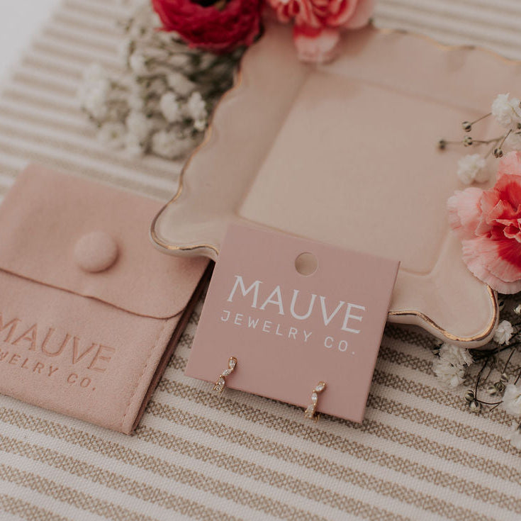 Mauve jewelry pouch and card on a striped fabric background with flowers.