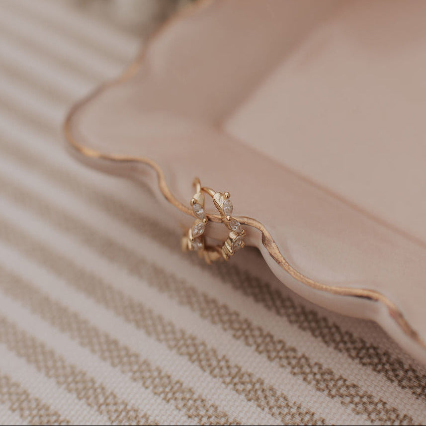 Gold earrings on a pink plate with flowers in the background