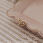 Gold earrings on a pink plate with flowers in the background