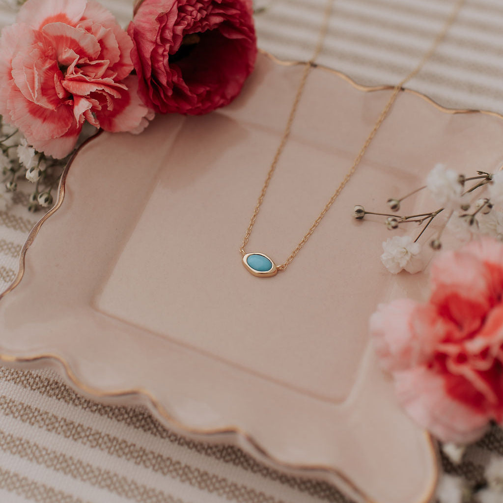 Gold necklace with a turquoise pendant on a decorative plate with flowers