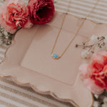 Load image into Gallery viewer, Gold necklace with a turquoise pendant on a decorative plate with flowers
