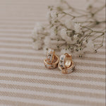 Pair of gold earrings on a striped fabric background with small white flowers.