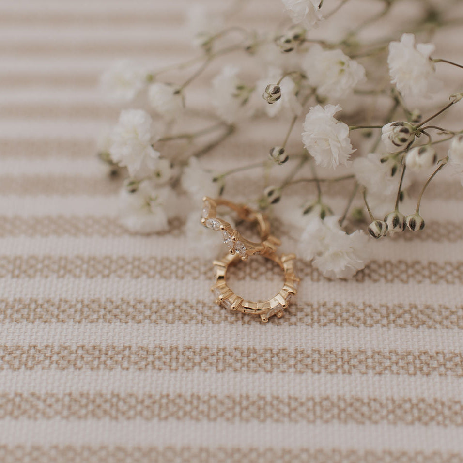 Gold earrings on a textured beige surface with small white flowers