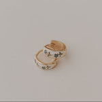 Load image into Gallery viewer, Two gold earrings with blue floral designs on a light beige background
