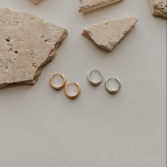 Gold earrings on a light gray surface with stone fragments