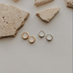 Gold earrings on a light gray surface with stone fragments