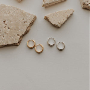 Gold earrings on a light gray surface with stone fragments
