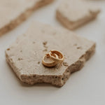 Two gold earrings on a textured stone surface with a blurred background