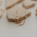 Two gold earrings on a textured stone surface