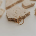 Load image into Gallery viewer, Two gold earrings on a textured stone surface
