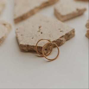 Two gold earrings on a textured stone surface