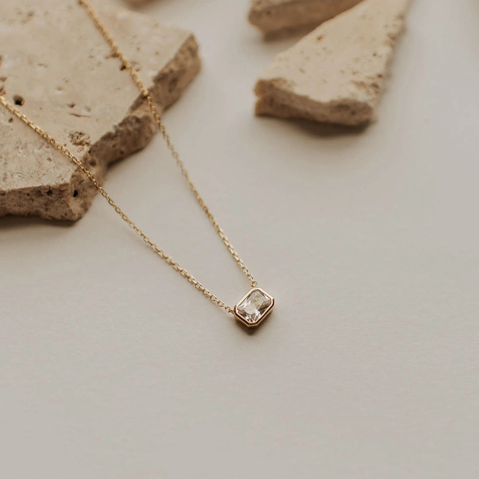 Gold necklace with a diamond pendant on a neutral background