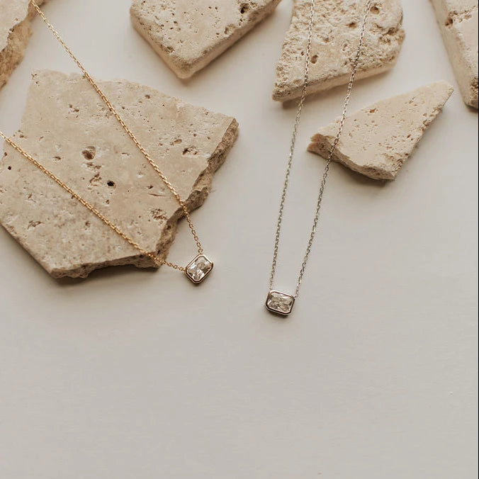 Two necklaces with square pendants on stone surfaces