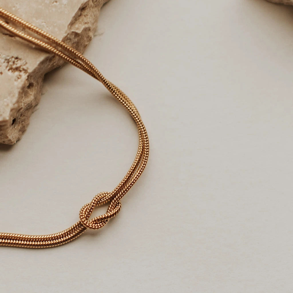Gold necklace with a knot design on a neutral background