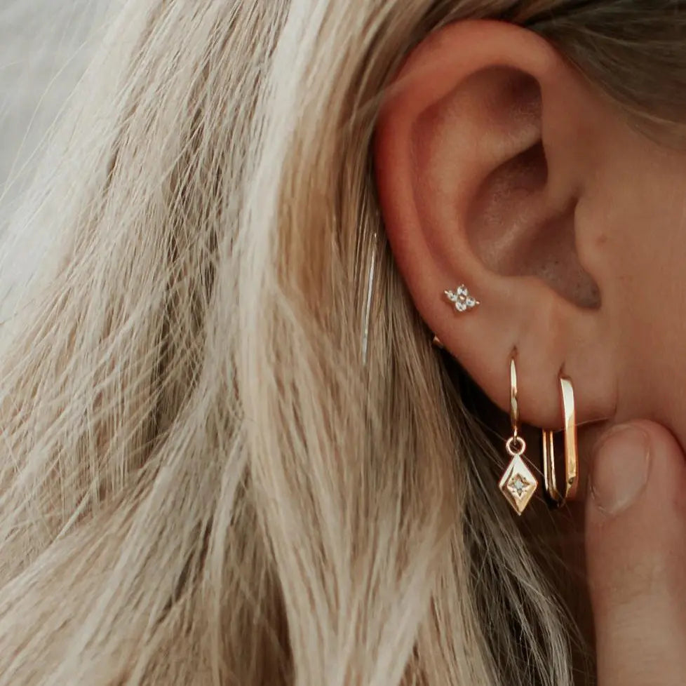 Close-up of an ear with gold hoop earrings and a small stud.
